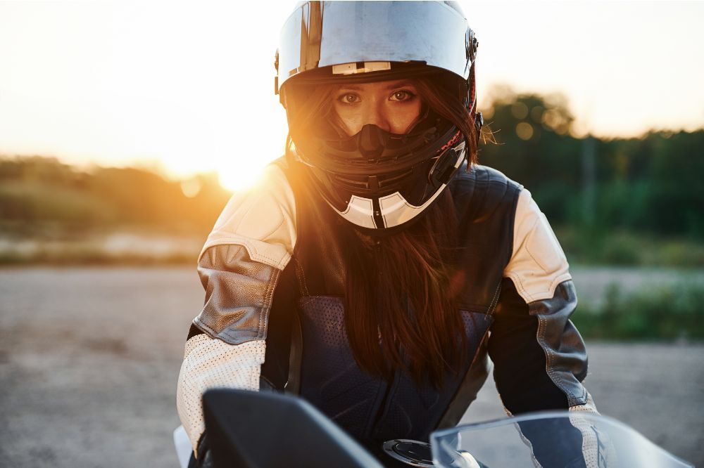 Žena s moto prilbou a koženou bundou sedí na motorke