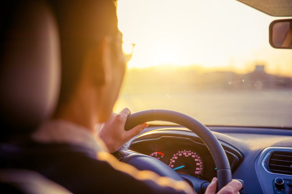 Muž šoféruje auto proti zapadajúcemu slnku