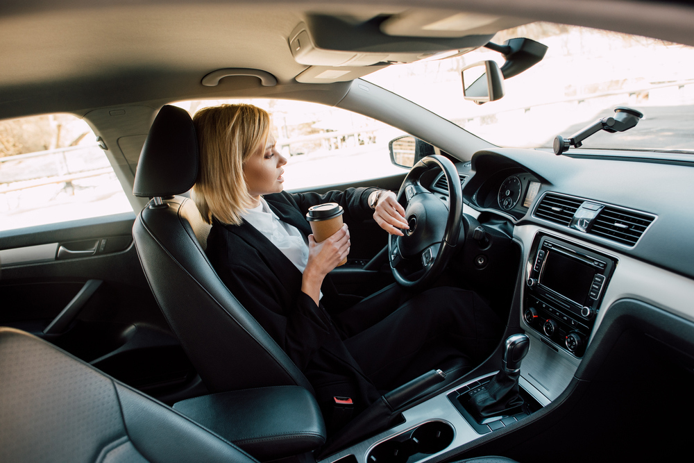 Žena za volantom s kávou v ruke 