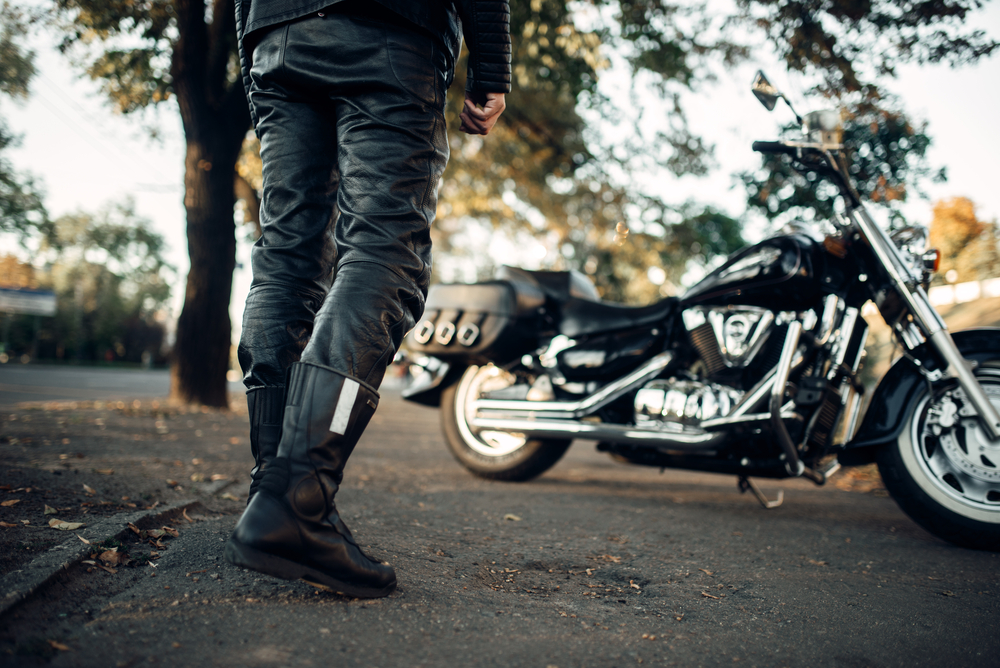 Čierna motocyklová obuv, nohavice a motorka v pozadí