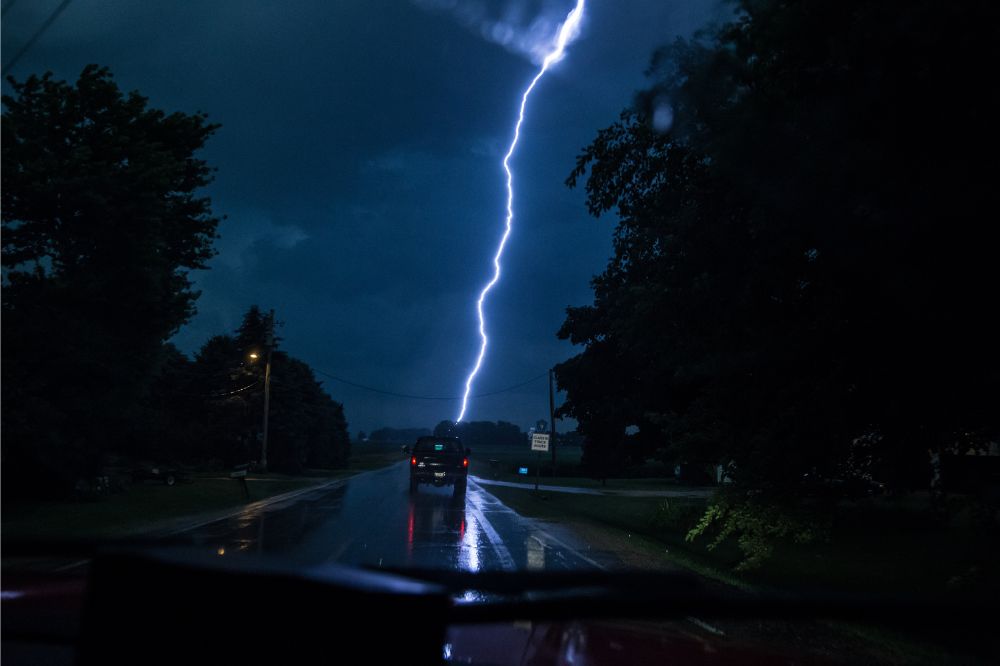 Auto ide po mokrej ceste počas búrky, keď je vidieť úder blesku