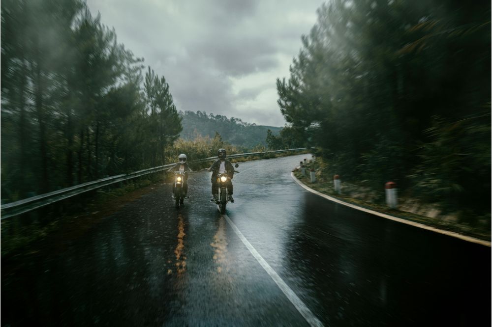 Dvaja motocyklisti jazdia v daždi po mokrej ceste